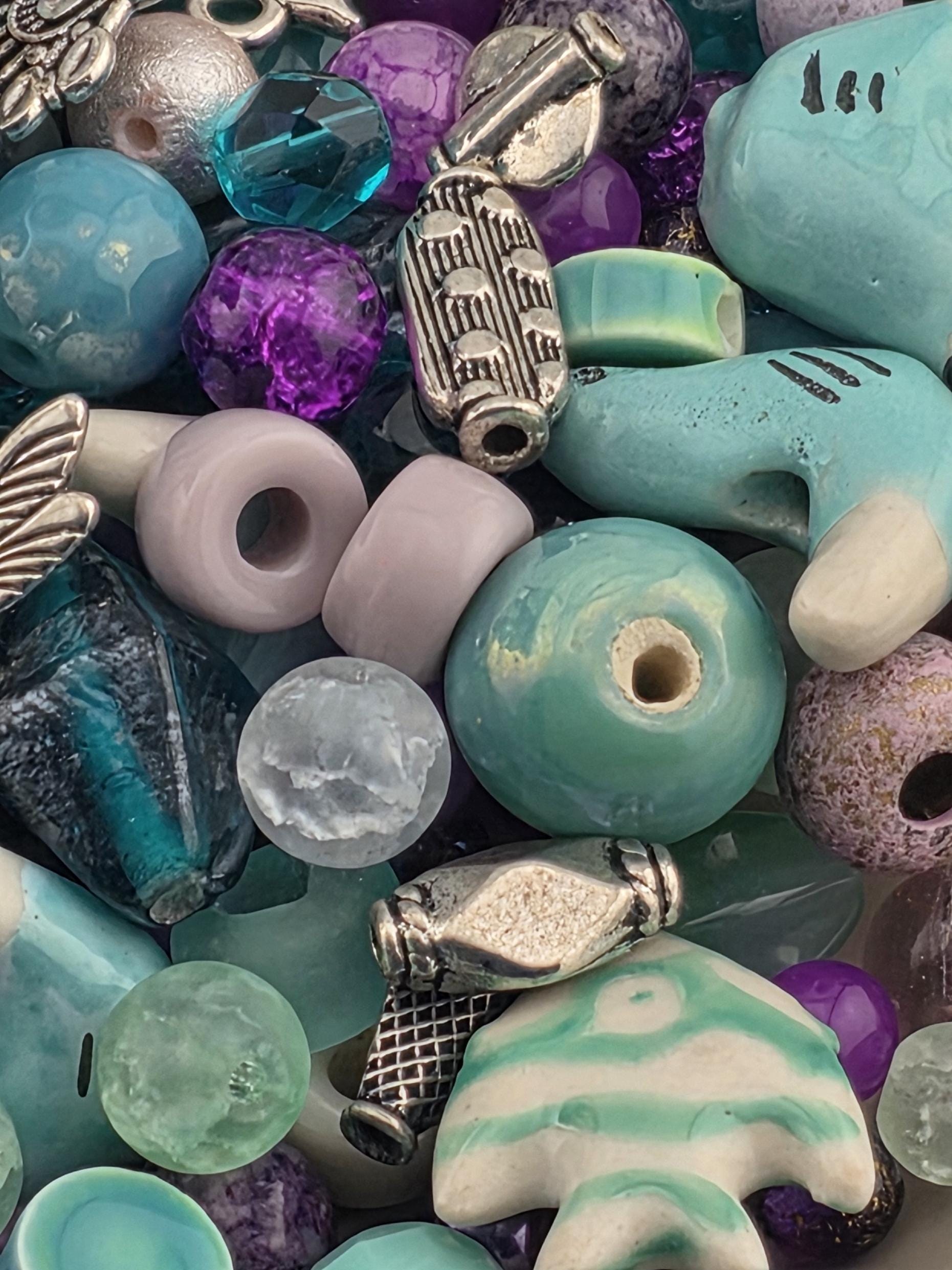 A colorful assortment of beads, charms, and other decorative items, including blue, green, purple, and silver elements, are scattered together.