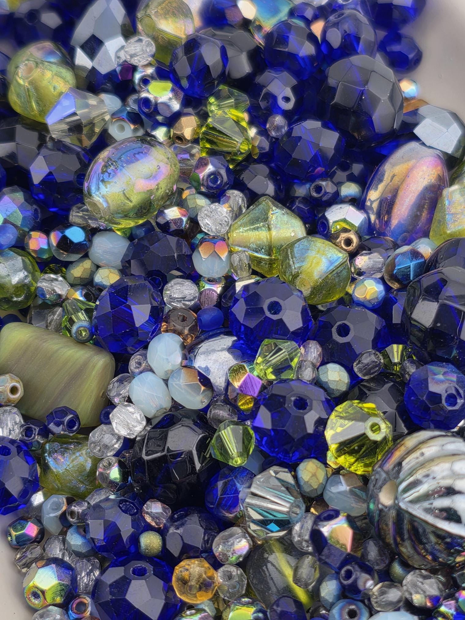 The image is a close-up of a collection of colorful glass beads, including blue, green, yellow, and silver beads, arranged in a visually appealing manner.