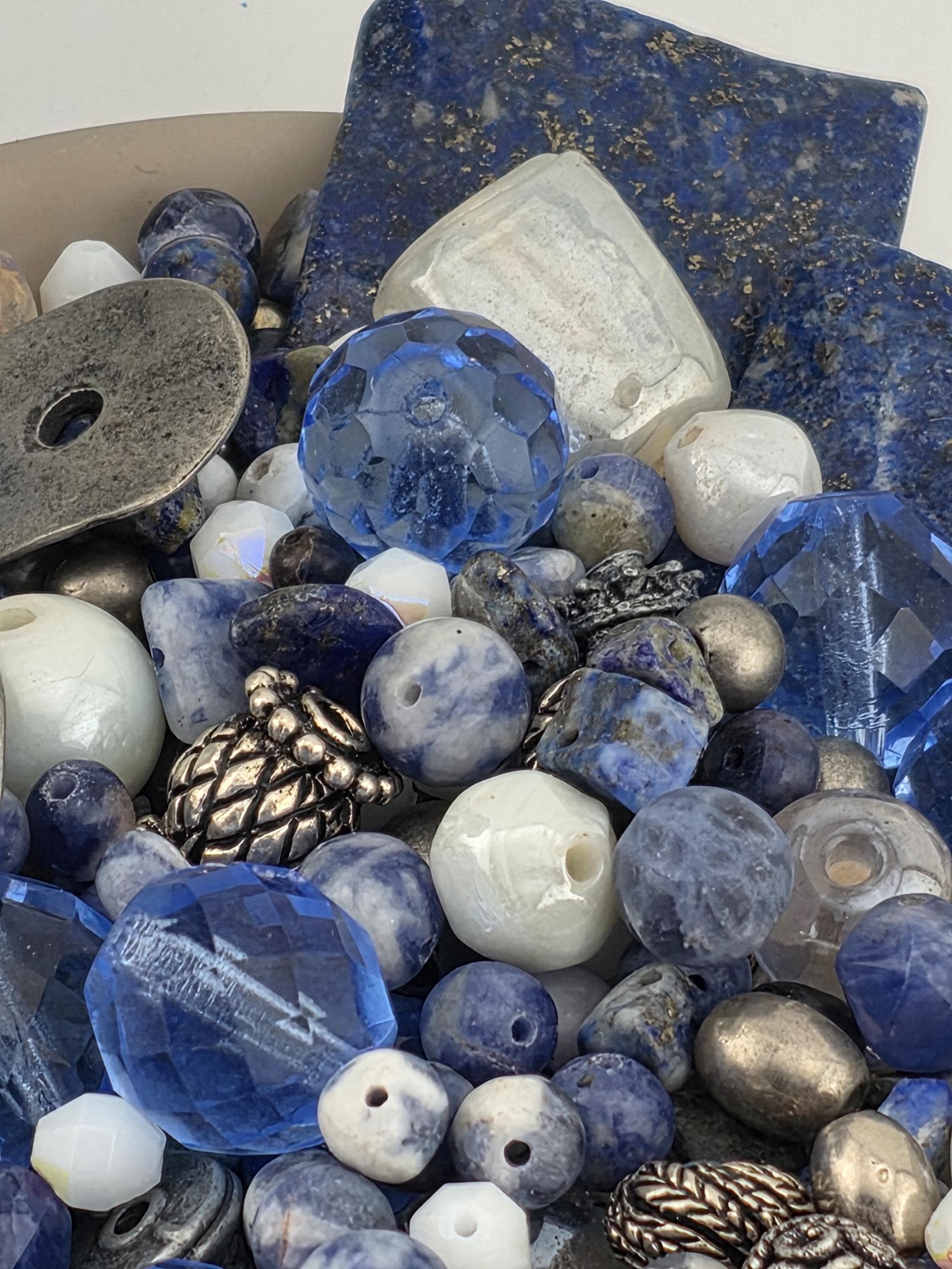 a variety of blue and silver beads, including clear and multicolored beads, as well as some metallic and textured beads. The arrangement of the beads creates a visually appealing and diverse collection.