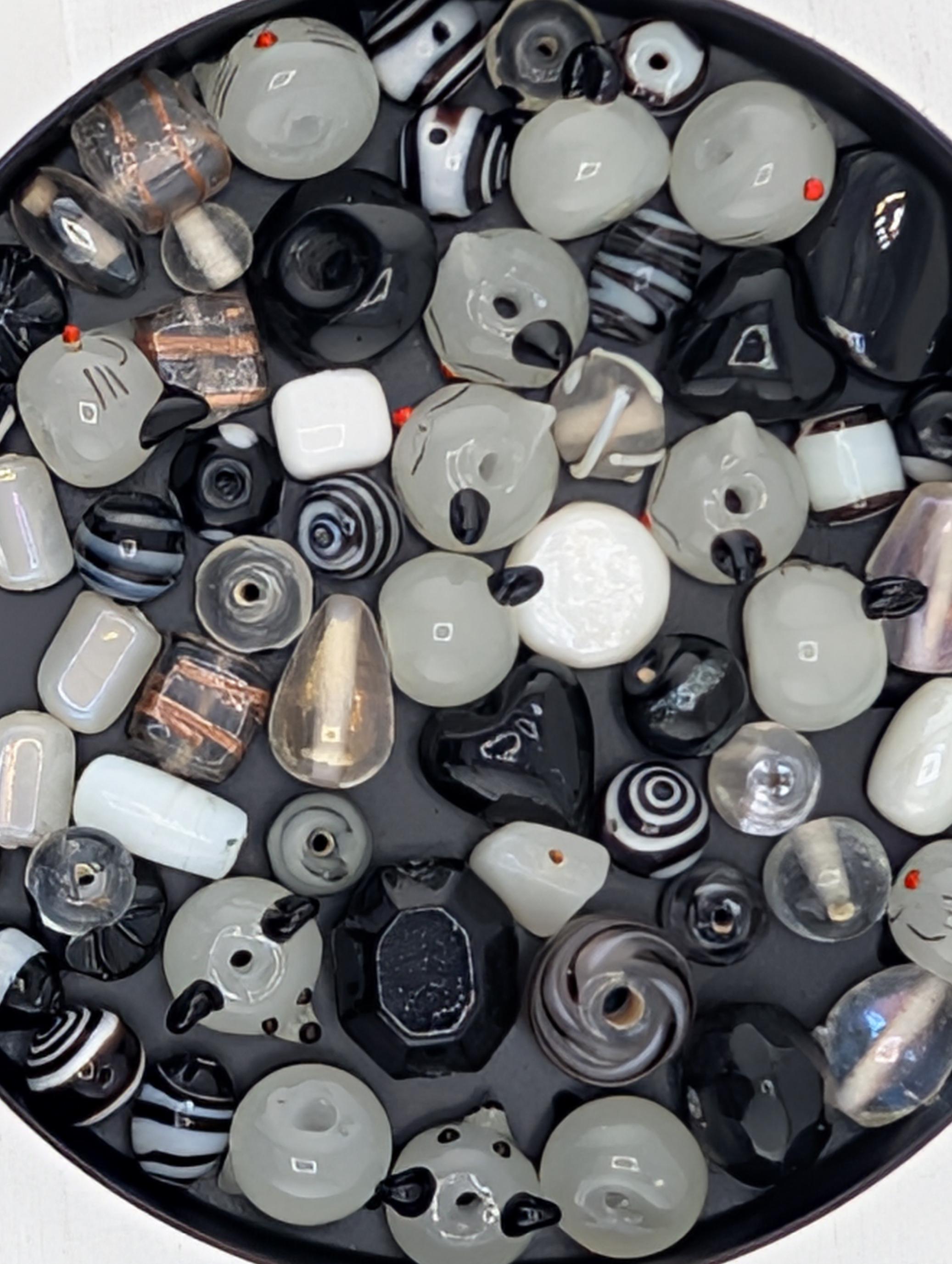a variety of glass beads in different shapes, sizes, and colors, including black, white, and silver, arranged in a circular pattern.