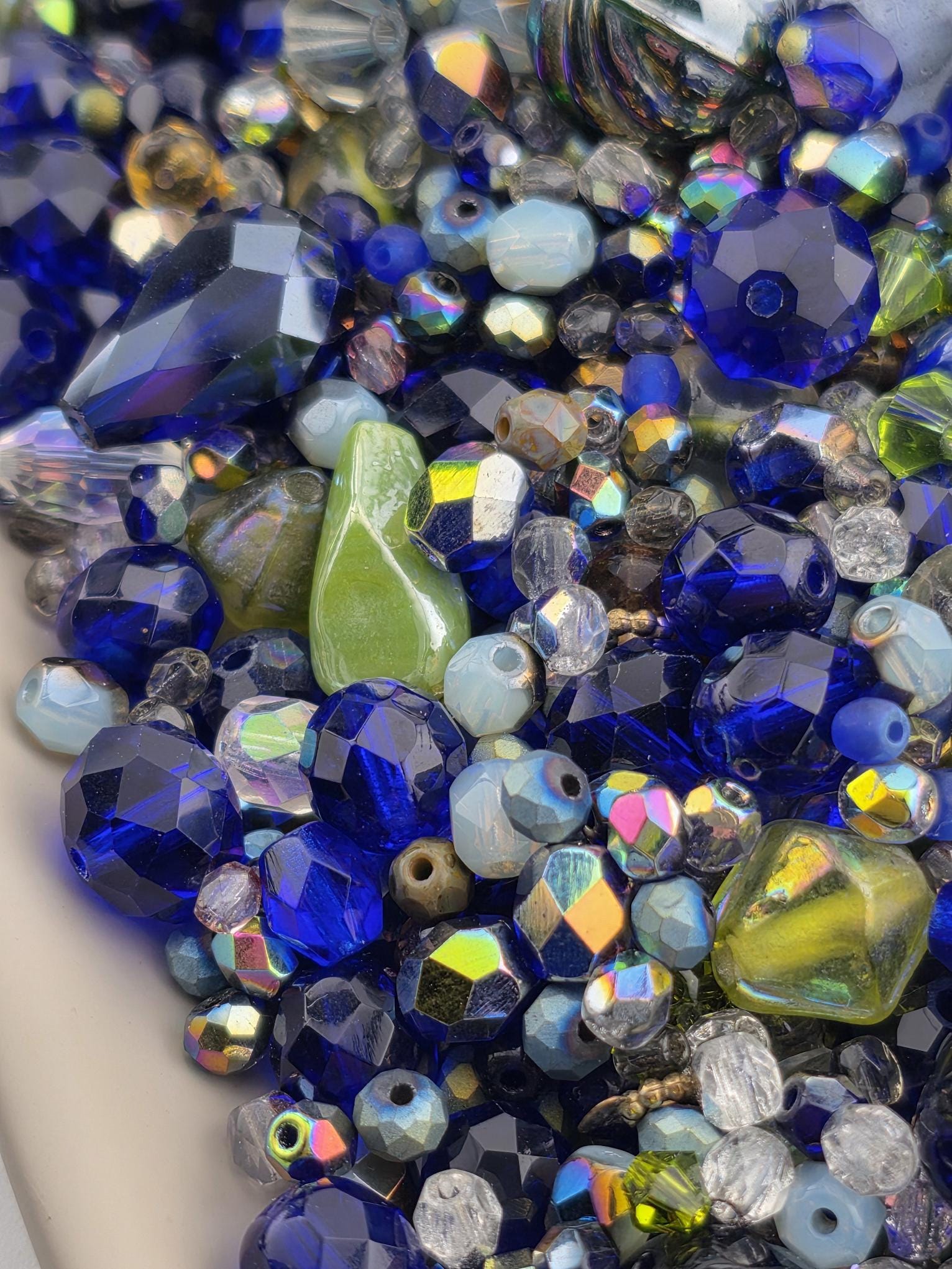 The image is a close-up of a collection of colorful glass beads, including blue, green, and yellow beads, as well as some clear beads. The beads are scattered and overlapping, creating a visually striking and vibrant display.