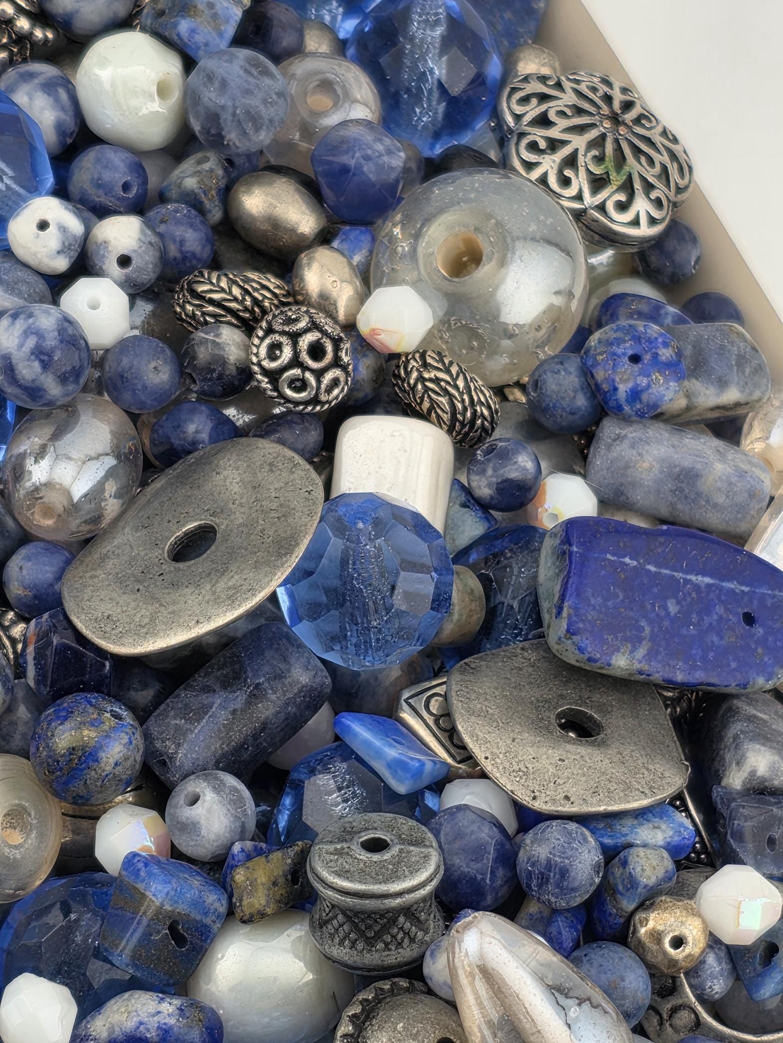 a variety of blue and silver beads, including clear and blue beads, as well as metal beads and beads with intricate designs. The beads are scattered throughout the frame, creating a visually interesting and diverse collection.