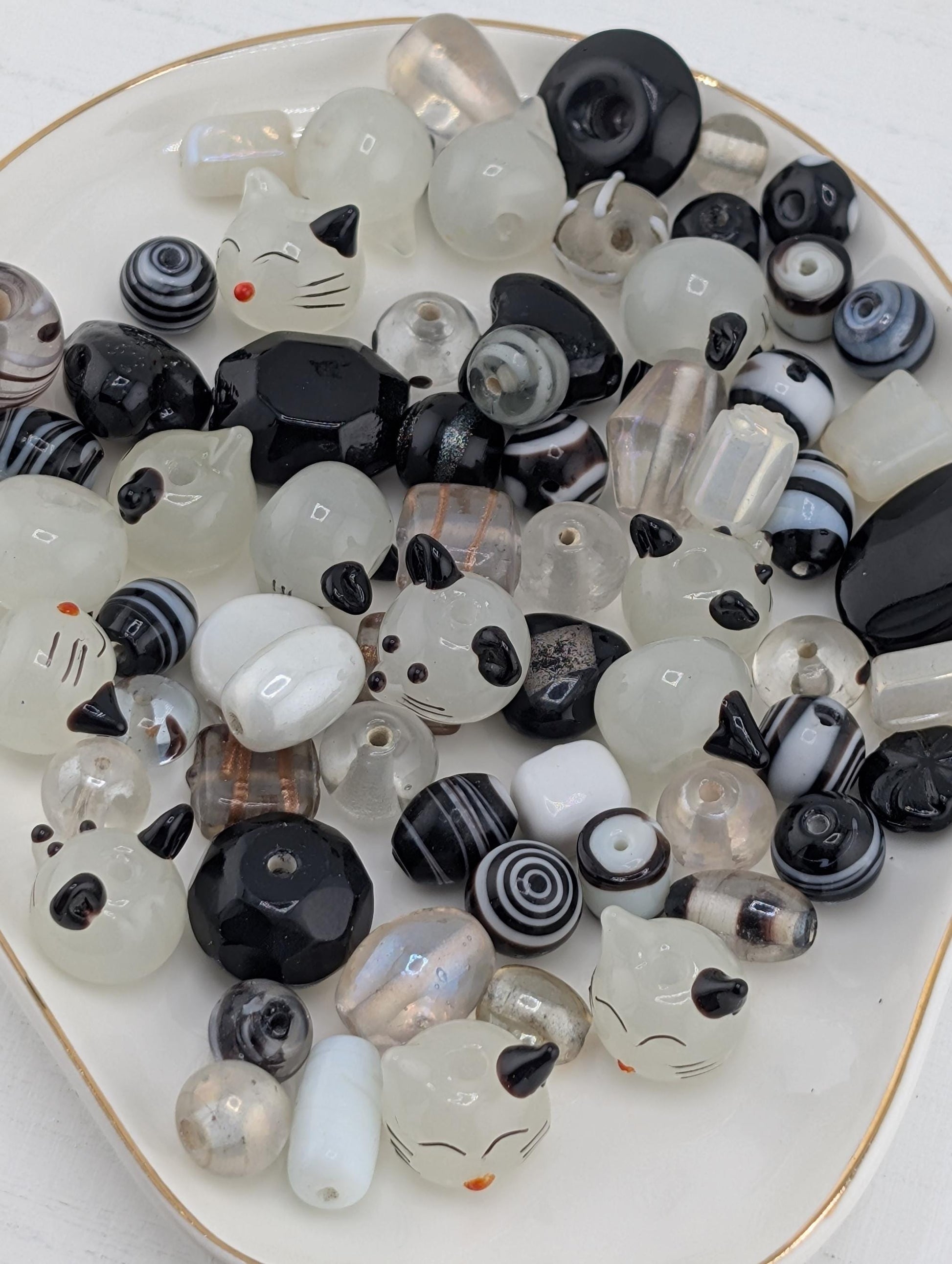 a collection of various glass beads, including black, white, and multicolored beads, arranged on a white plate with a gold rim.