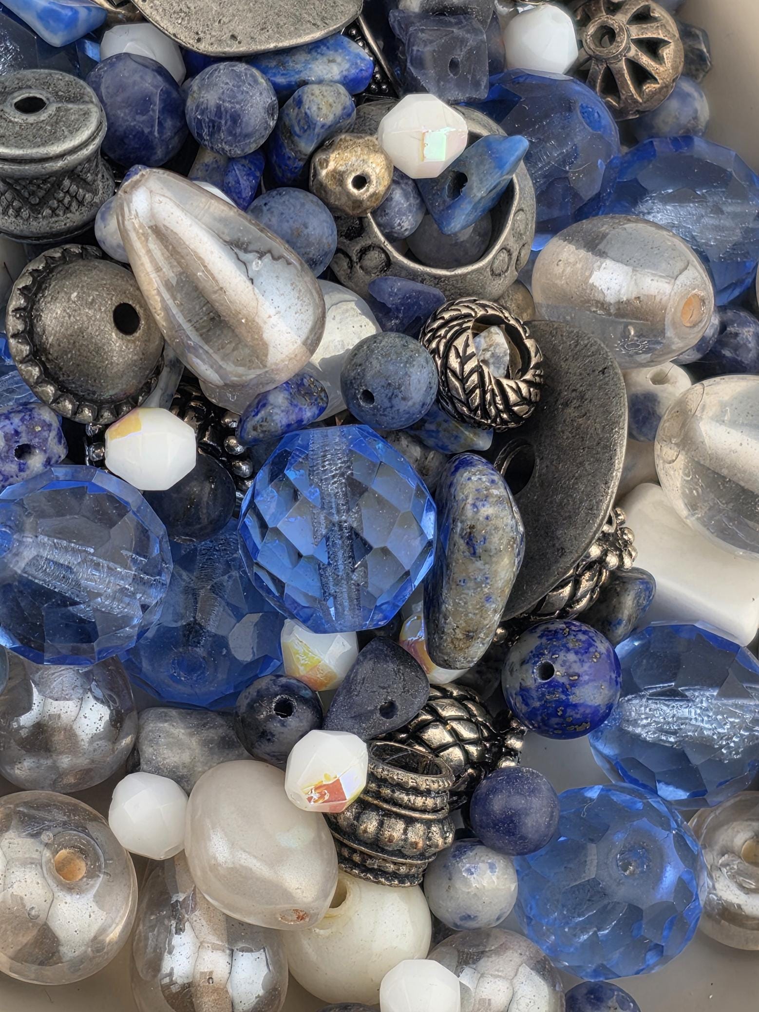 a variety of colorful glass beads and metal pieces, including clear, blue, and silver beads, as well as metal beads and metal pieces.