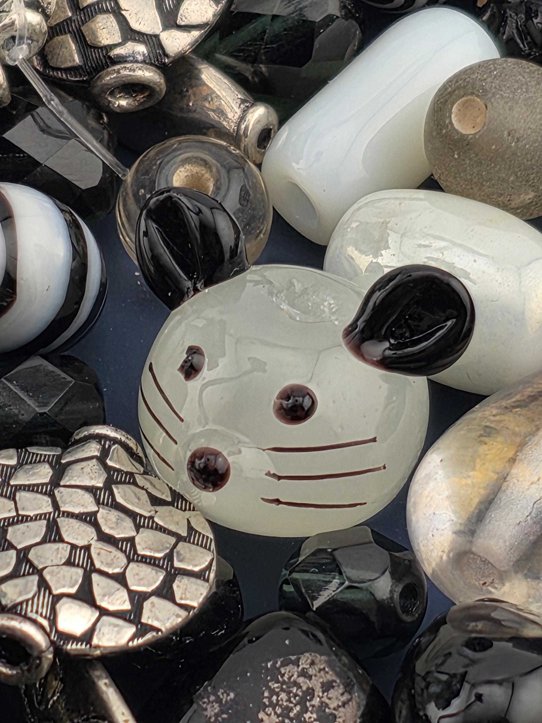 a variety of colorful glass beads and metal objects, including a white and black glass bead with a black dot pattern, a white and black glass bead with a black dot pattern, and a silver and black glass bead with a geometric pattern.