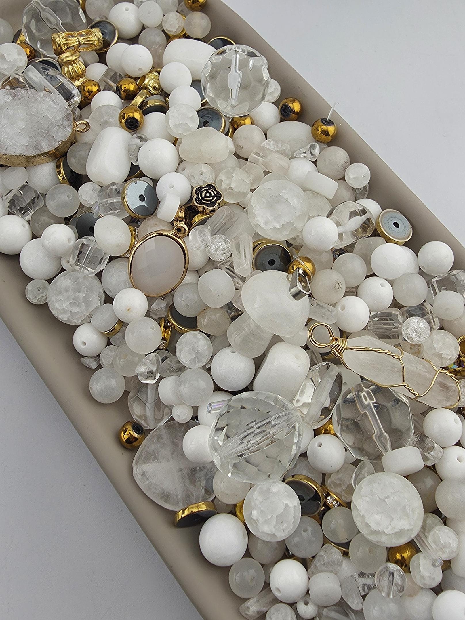 The image is a collection of various beads and jewelry pieces, including clear beads, gold beads, and other decorative elements, arranged in a visually appealing manner.