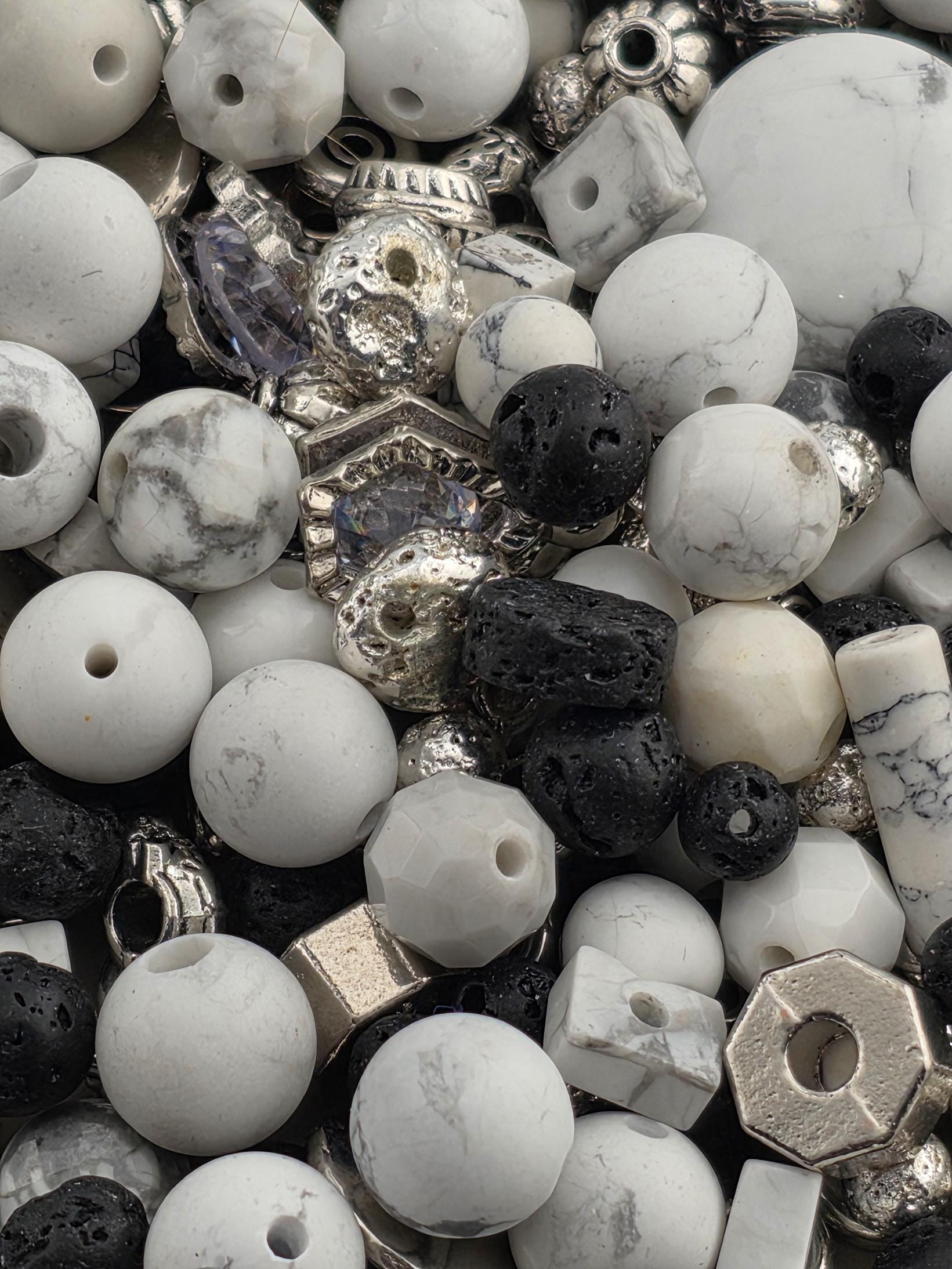 The image is a close-up of various beads and metal pieces, including white, black, and silver beads, as well as metal components.