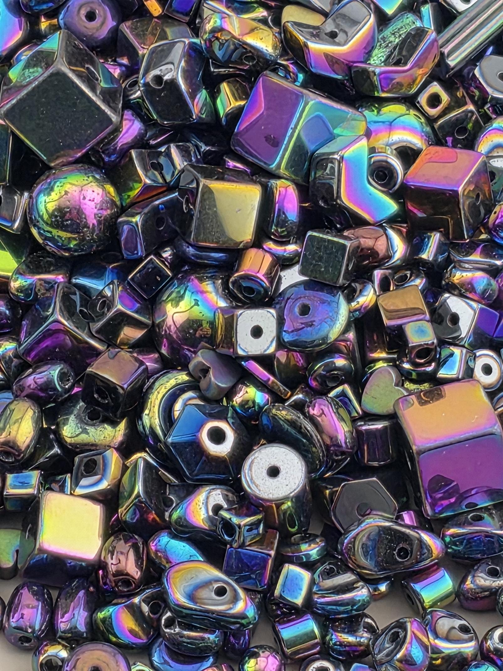 The image is a close-up of a collection of colorful, iridescent beads and shapes, including cubes, spheres, and other geometric forms, creating a visually striking and vibrant display.