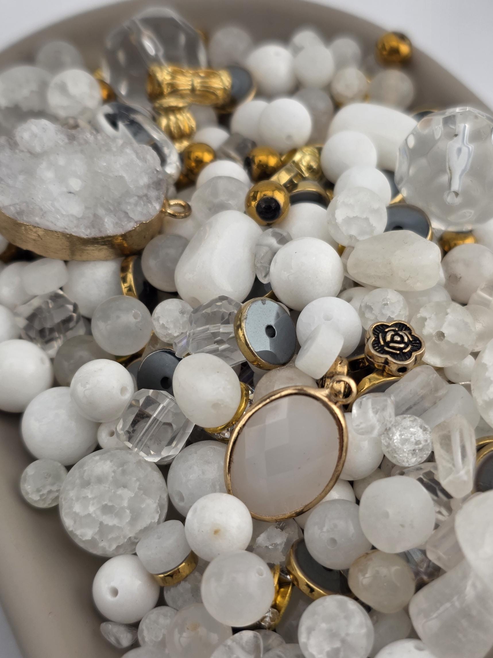 The image is a close-up of a collection of various beads, charms, and pendants, including clear beads, gemstones, and metal pieces.