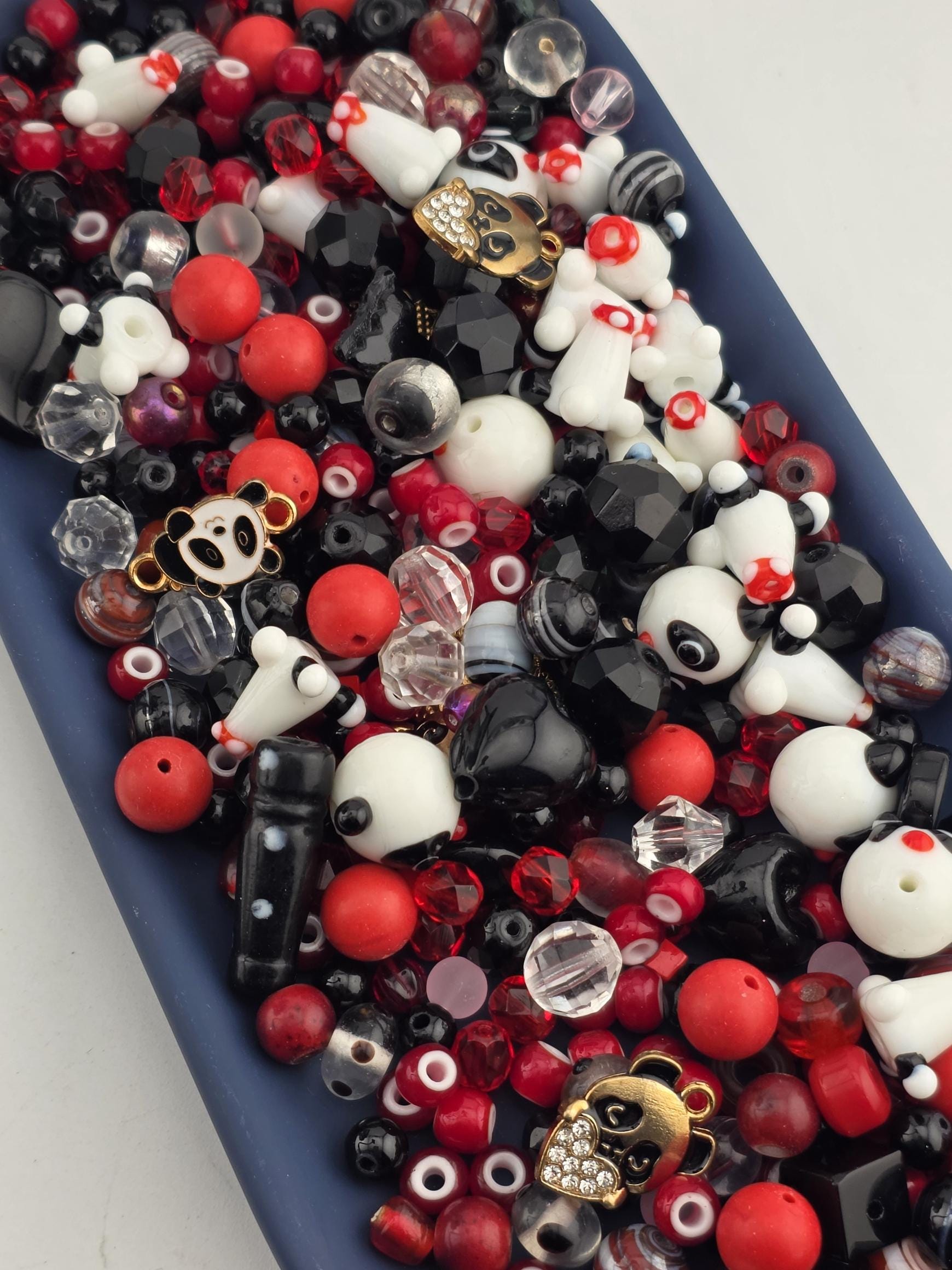 A collection of various beads, charms, and beads in different colors, including red, black, white, and gold, arranged on a blue surface.