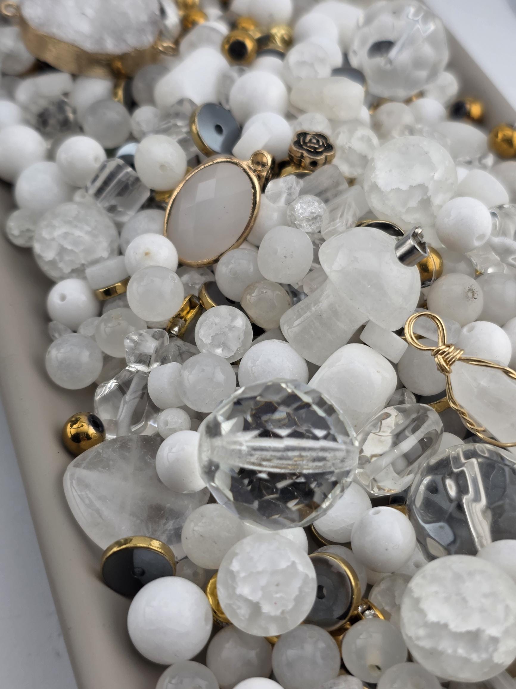 The image is a close-up of various crystal beads and gemstones, including clear and white stones, as well as some metallic and gold-colored elements.