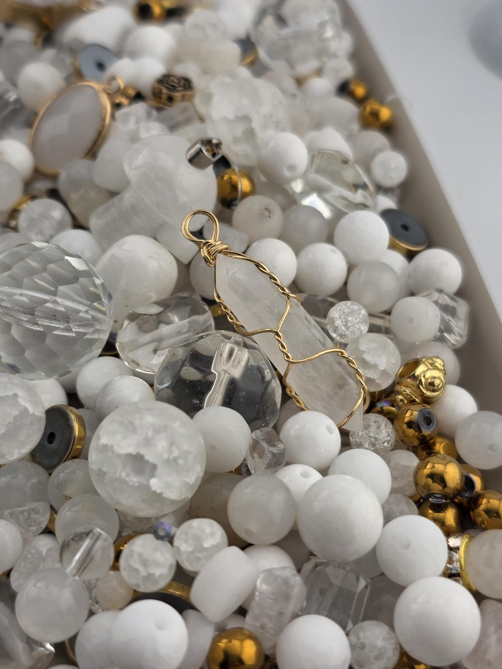 The image is a close-up of various crystal beads and gemstones, including clear and white beads, as well as some with a metallic or gold finish.