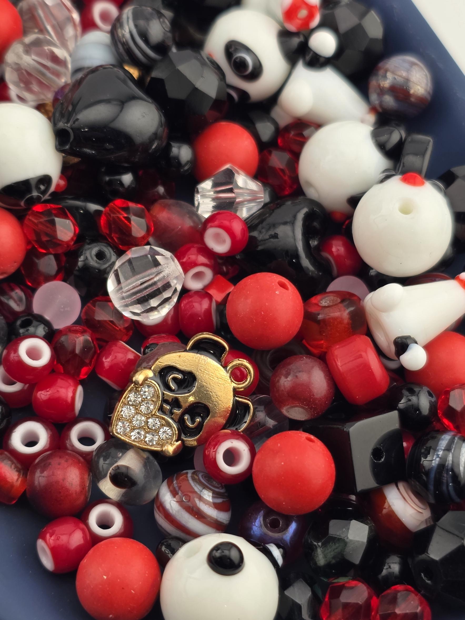 A close-up image of a collection of colorful beads, charms, and beads in various shapes and sizes, including red, black, and white beads, as well as some with gemstones or crystals.