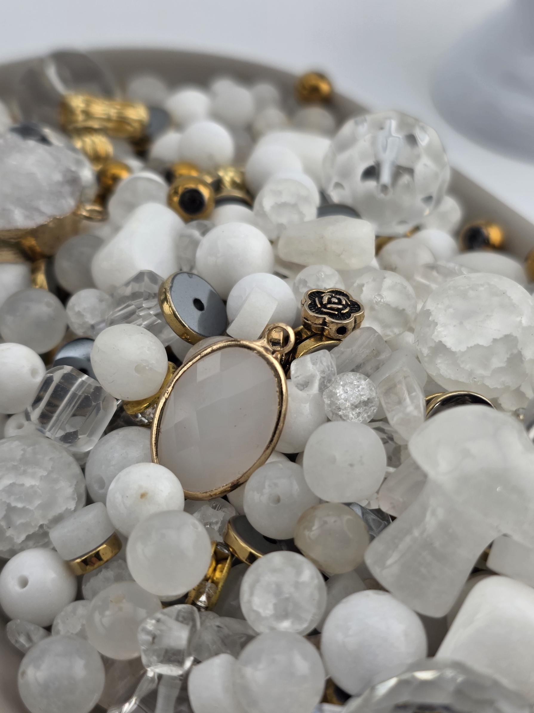 a close-up view of a collection of various beads, charms, and pendants in shades of white and gold.