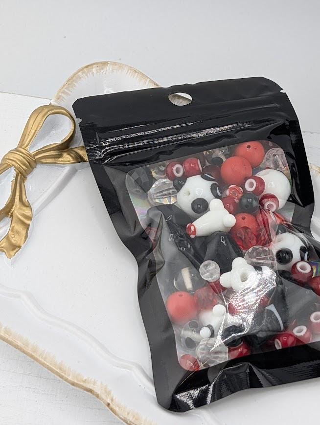 A clear plastic bag filled with various colorful beads, including red, white, and black beads, is placed on a white surface.