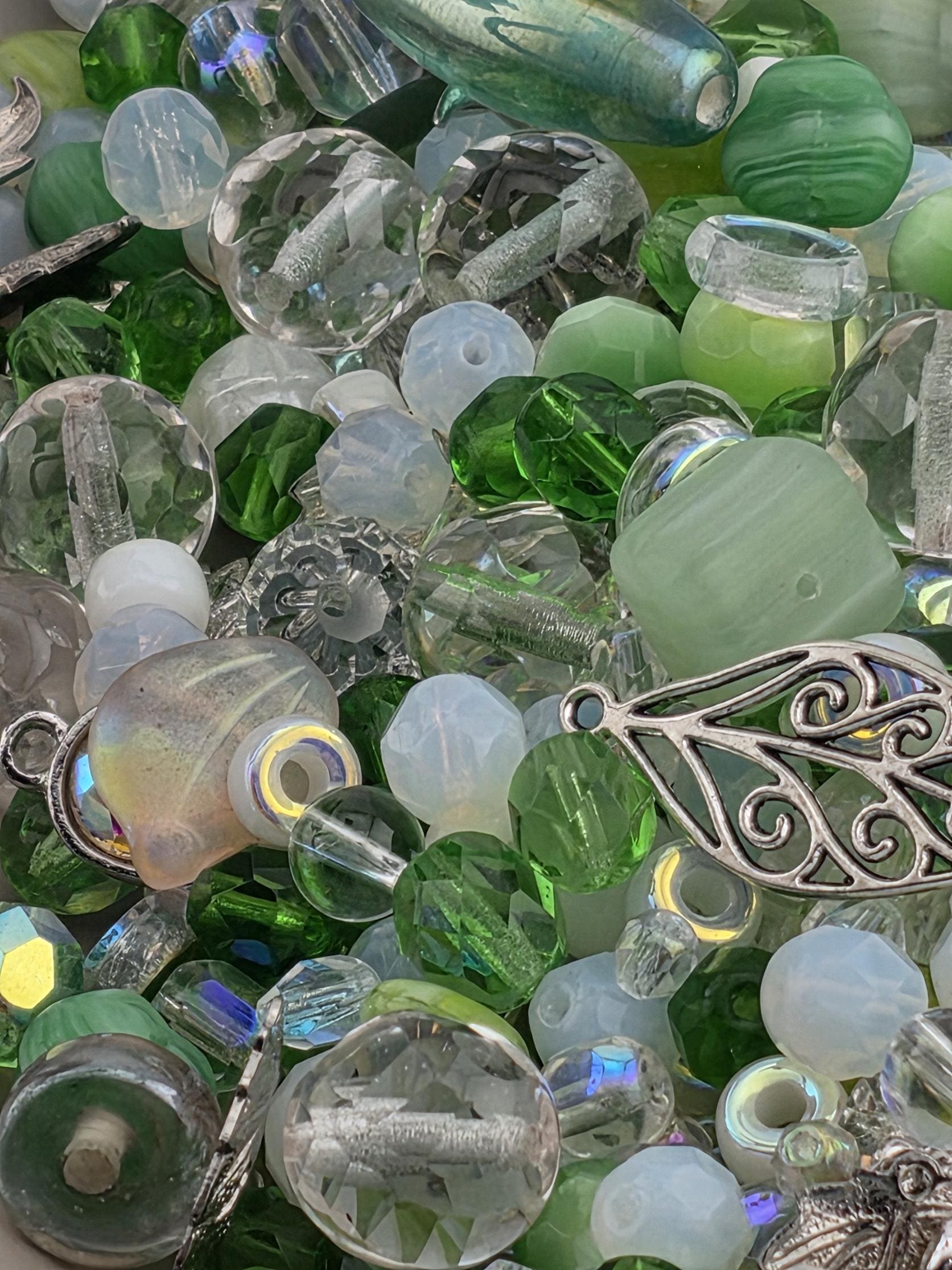The image is a close-up of various glass beads and charms in shades of green, white, and silver.