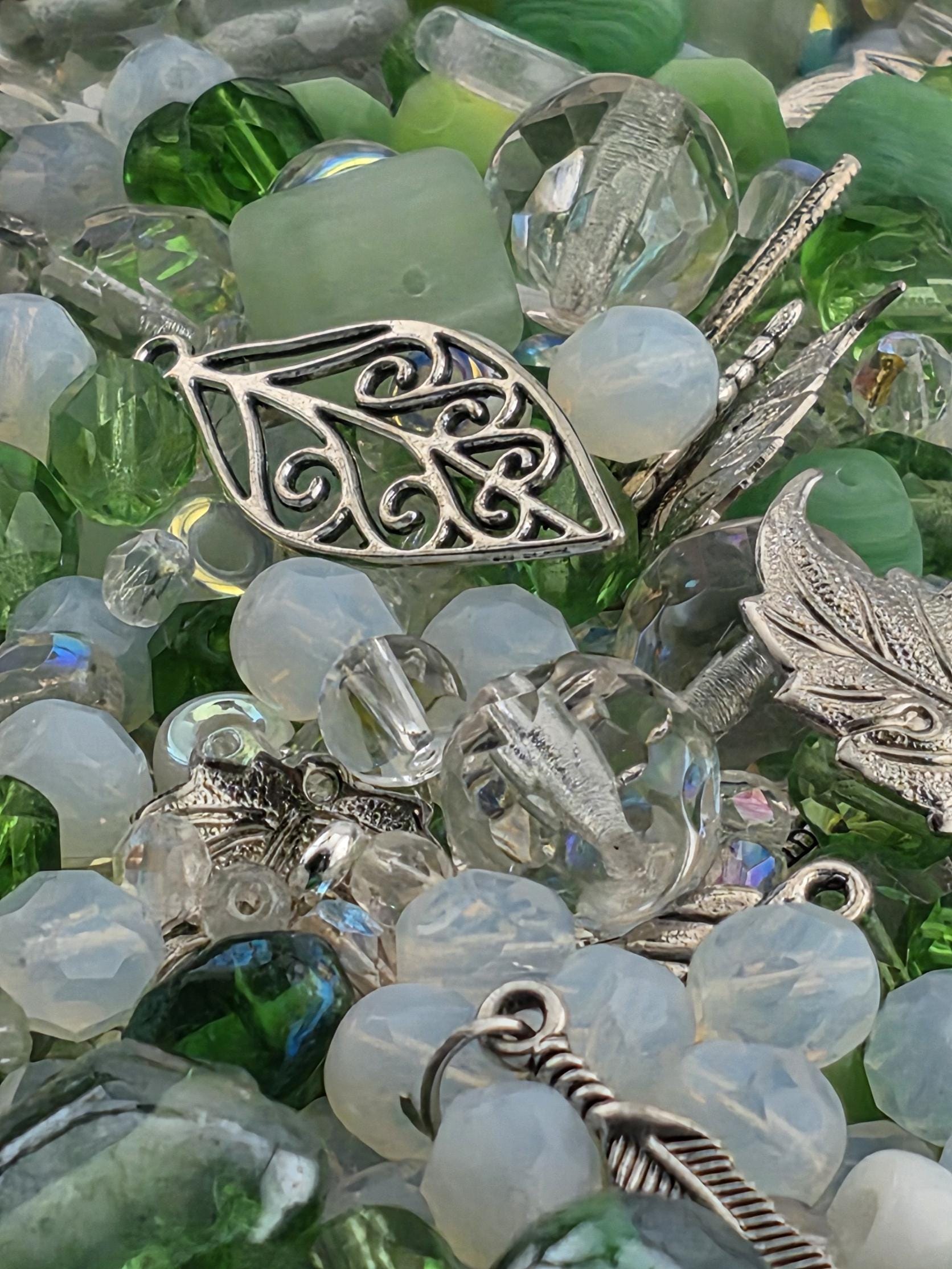 The image is a close-up of various colorful beads and charms, including clear and silver beads, as well as some leaf-shaped charms.