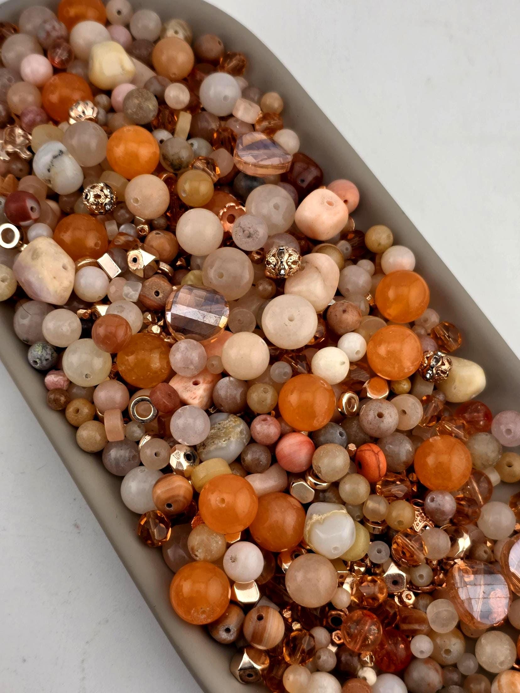 A collection of various beads and gemstones in shades of orange, beige, and brown, arranged in a container.