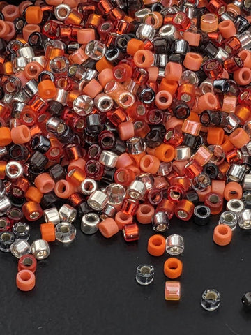 A pile of multicolored beads, including orange, black, and silver, scattered on a dark surface.