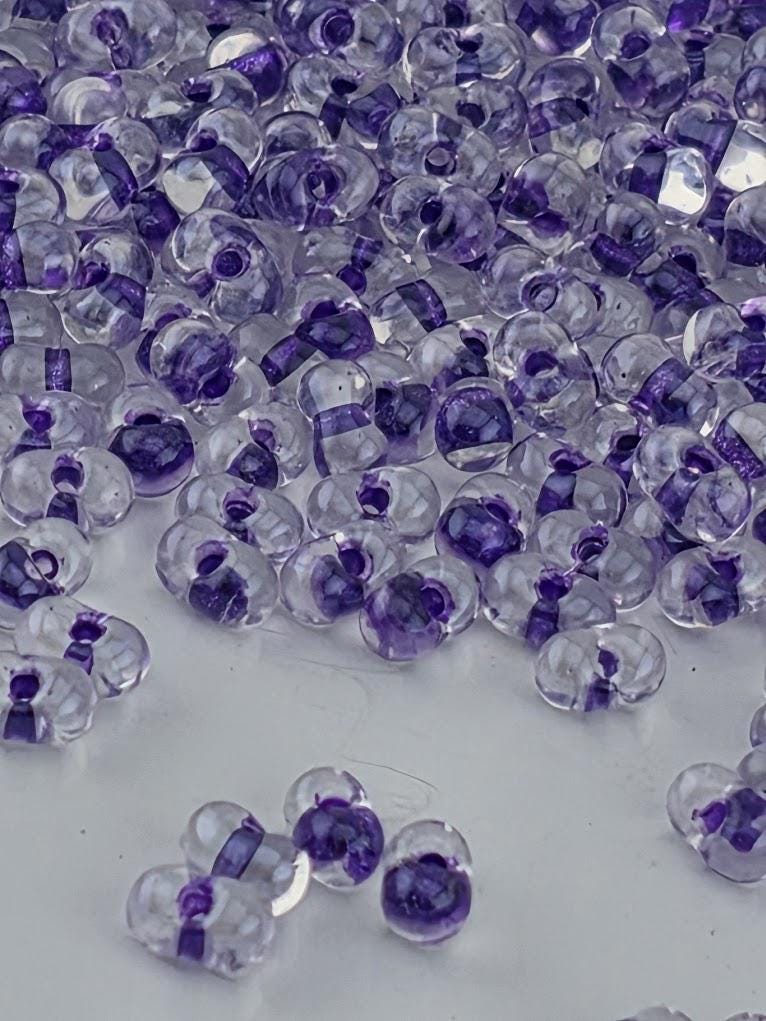 a collection of clear glass beads in various shades of purple, scattered across a white surface.