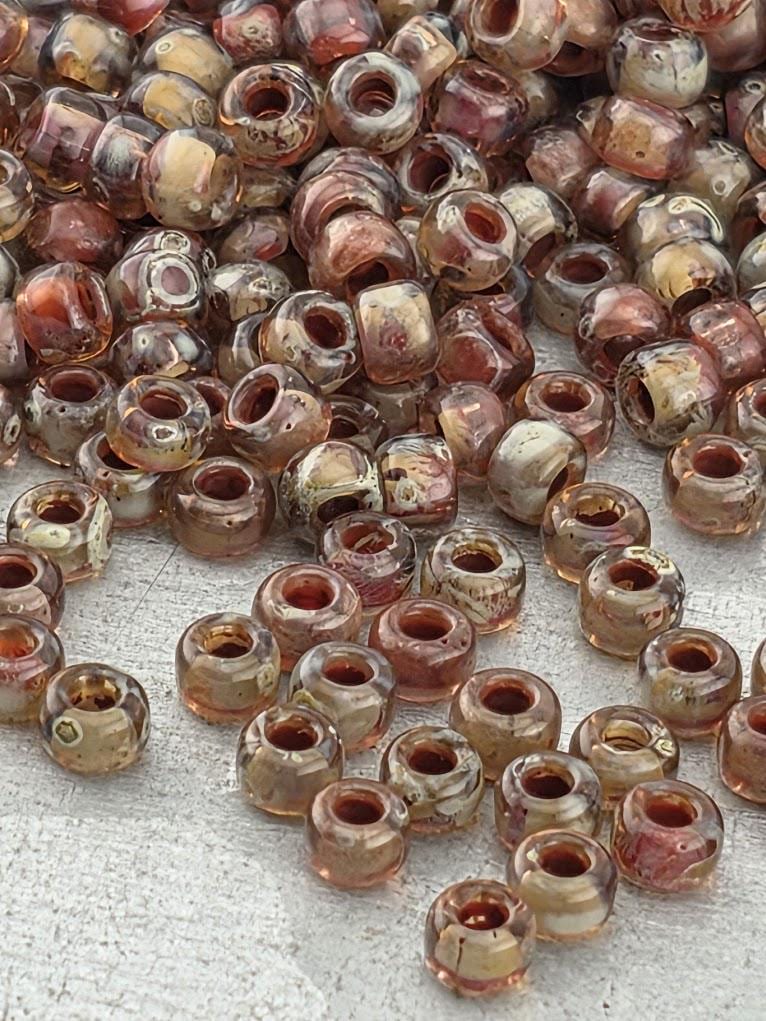 a large pile of glass beads in various colors, including shades of brown, beige, and orange, scattered on a surface.