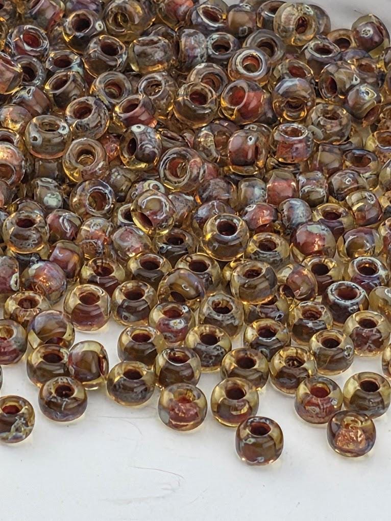 a large pile of small, clear glass beads in various colors, including yellow, orange, and red, scattered on a dark surface.