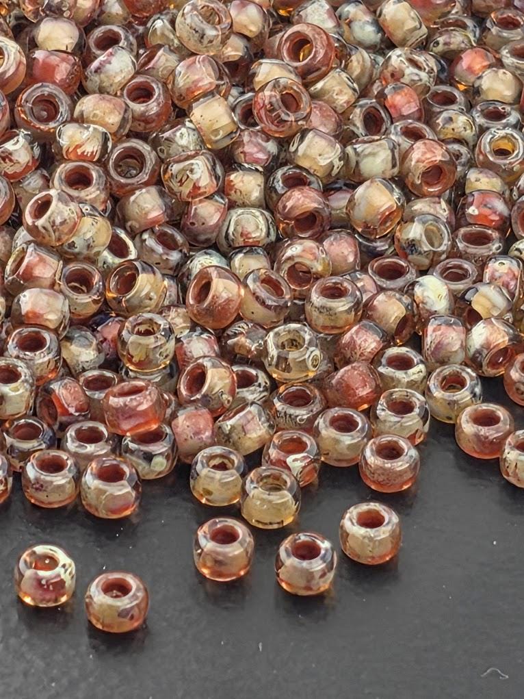 a large pile of small, clear beads in various colors, including shades of orange, beige, and brown, scattered across a dark surface.