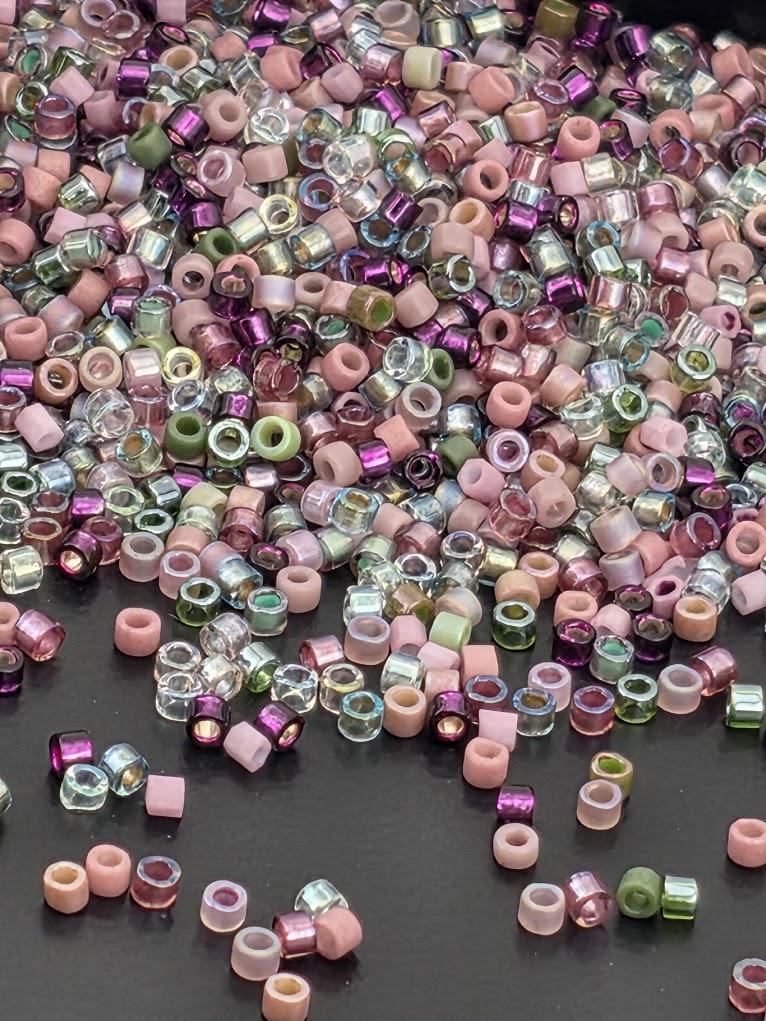 A large pile of multicolored beads, including clear and colored glass beads, scattered on a dark surface.