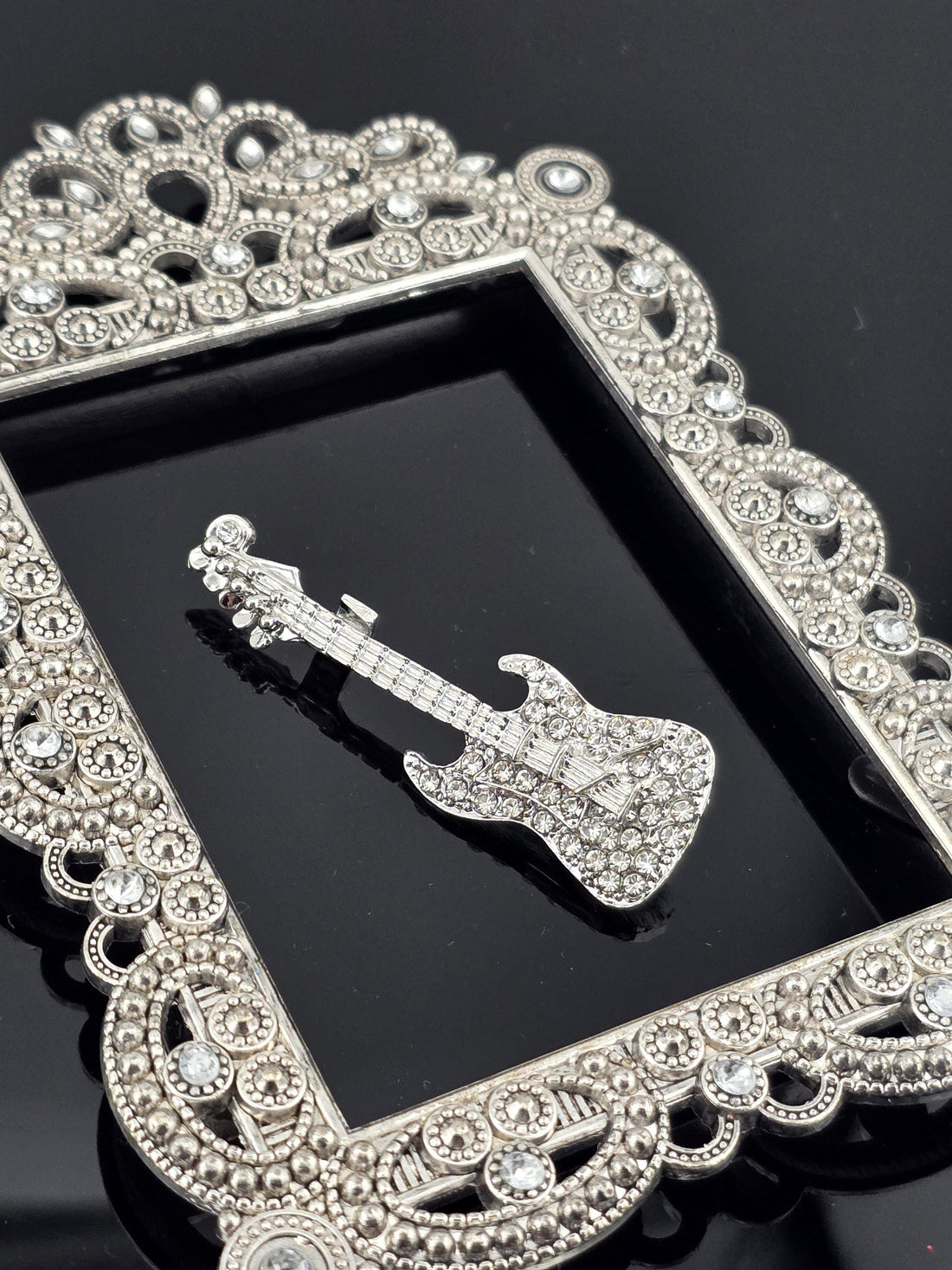 A silver-colored brooch with a diamond-encrusted frame is displayed against a black background.