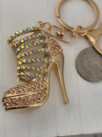 A gold-colored high-heeled shoe keychain with rhinestones and a coin keychain are placed on a white surface.