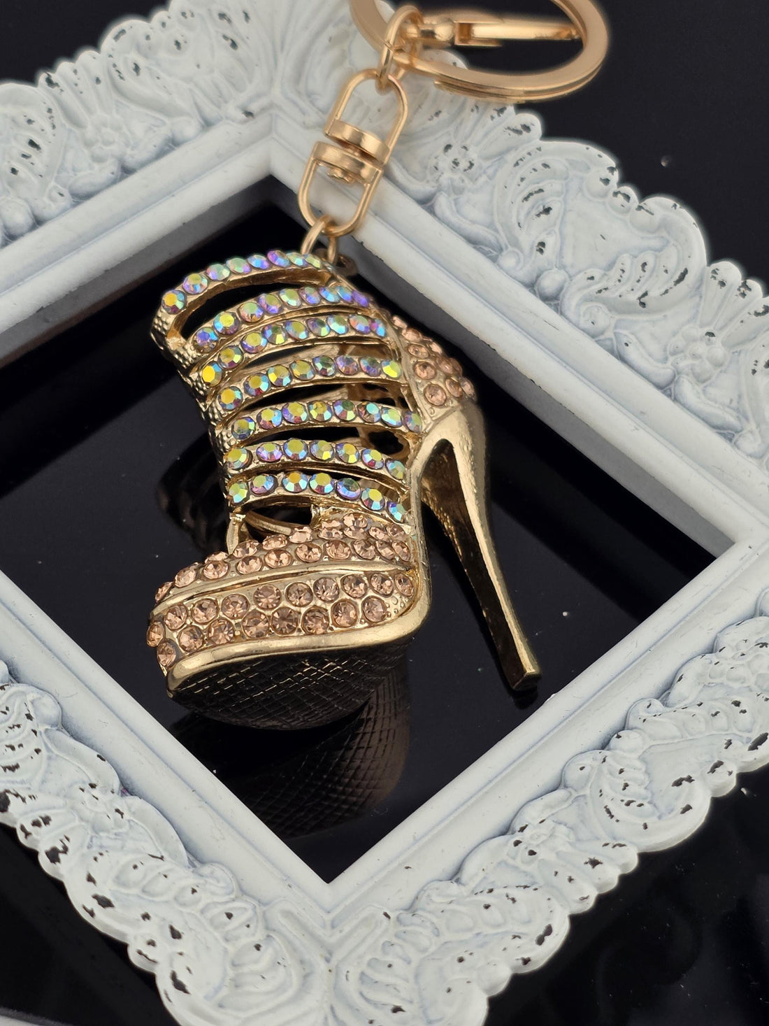 A gold-colored high-heeled shoe keychain with rhinestones and a coin keychain are placed on a white surface.