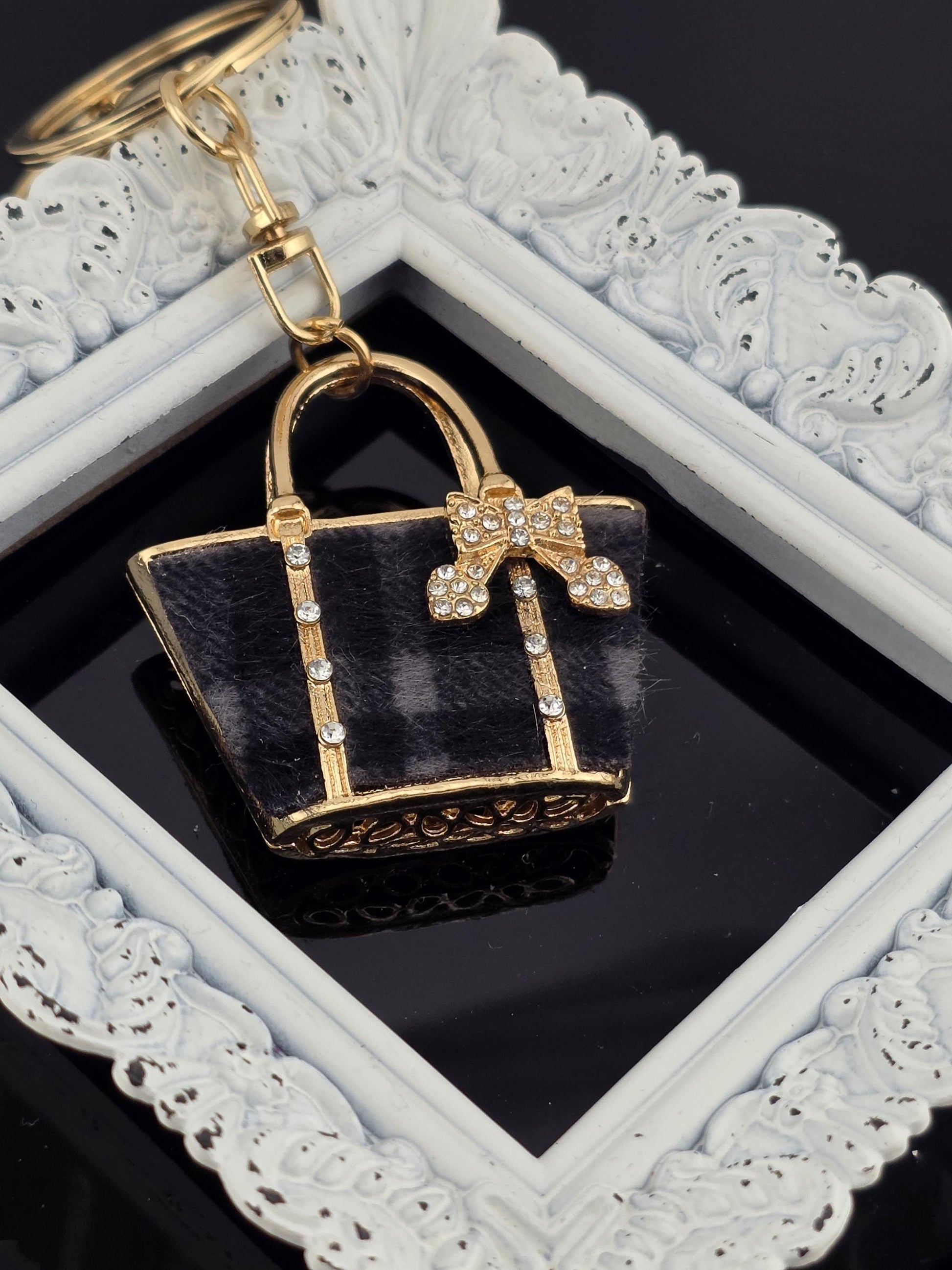 A small, ornate keychain in the shape of a handbag with a gold-colored frame and a decorative bow on the front.