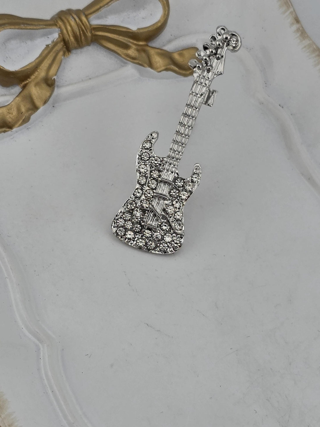 A silver-colored brooch with a diamond-encrusted frame is displayed against a black background.