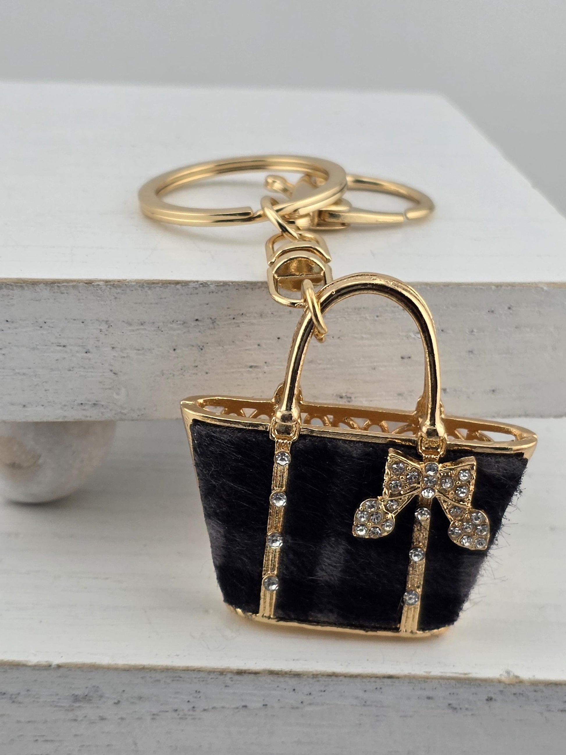 A gold-colored keychain with a black fur-like material and a gold bow on it, attached to a white surface.