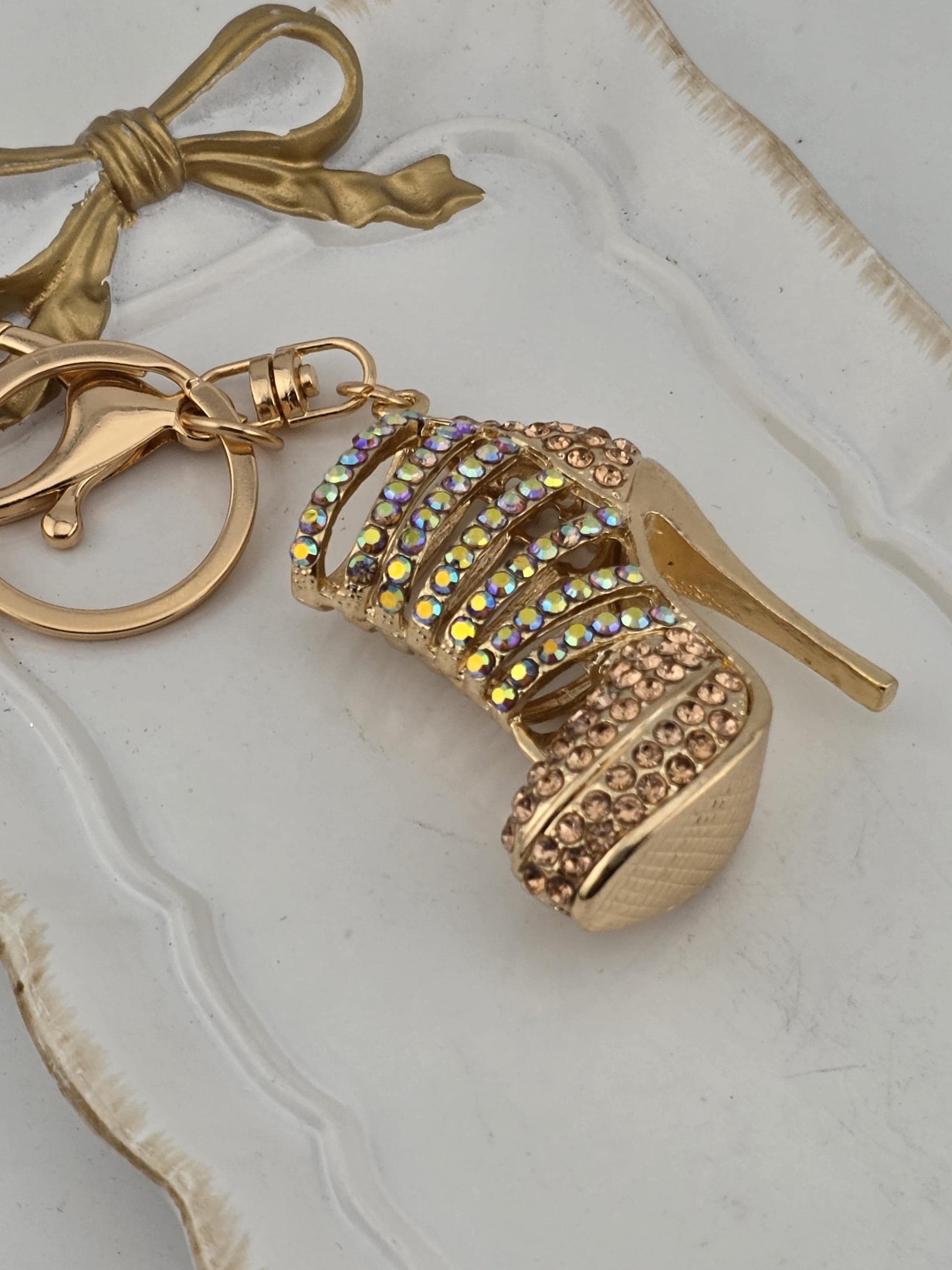 A gold-colored high-heeled shoe keychain with rhinestones and a gold-colored bow charm.