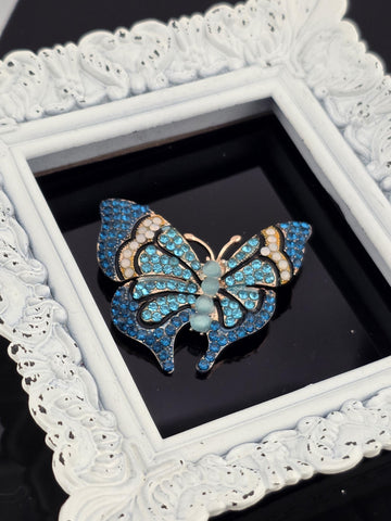 A decorative white frame with a blue and gold butterfly brooch with blue and white gemstones set in it.