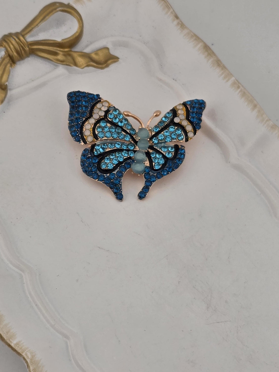 A decorative white frame with a blue and gold butterfly brooch with blue and white gemstones set in it.