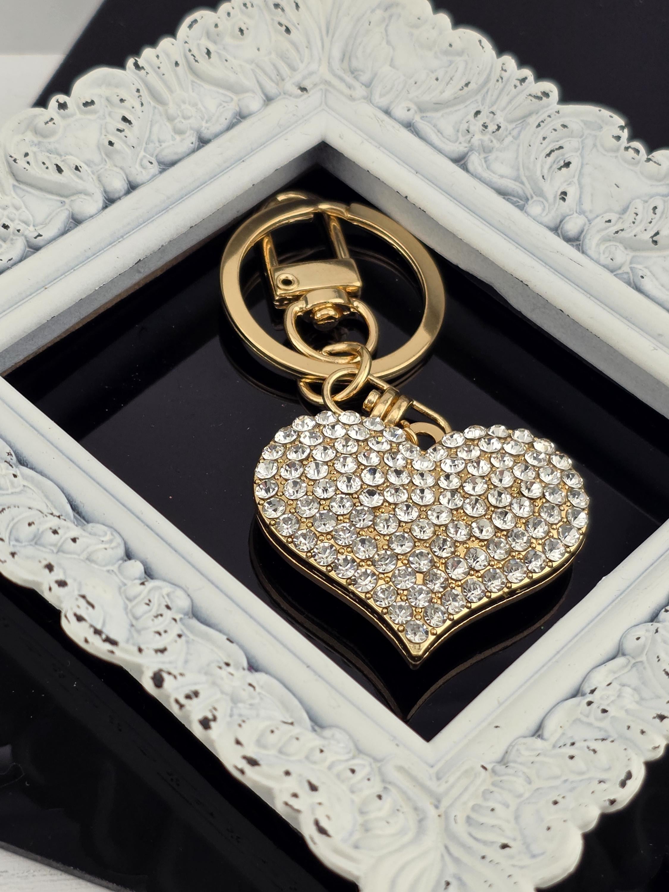 A heart-shaped pendant with sparkling rhinestones is displayed in a white ornate frame.