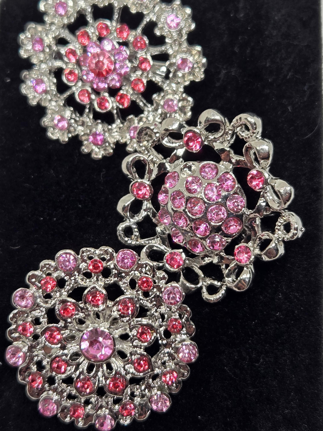three ornate brooches with intricate designs and sparkling pink gemstones.
