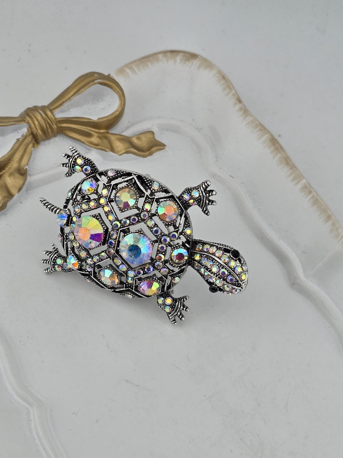 A decorative silver frame with a crystal turtle brooch is displayed against a dark background.