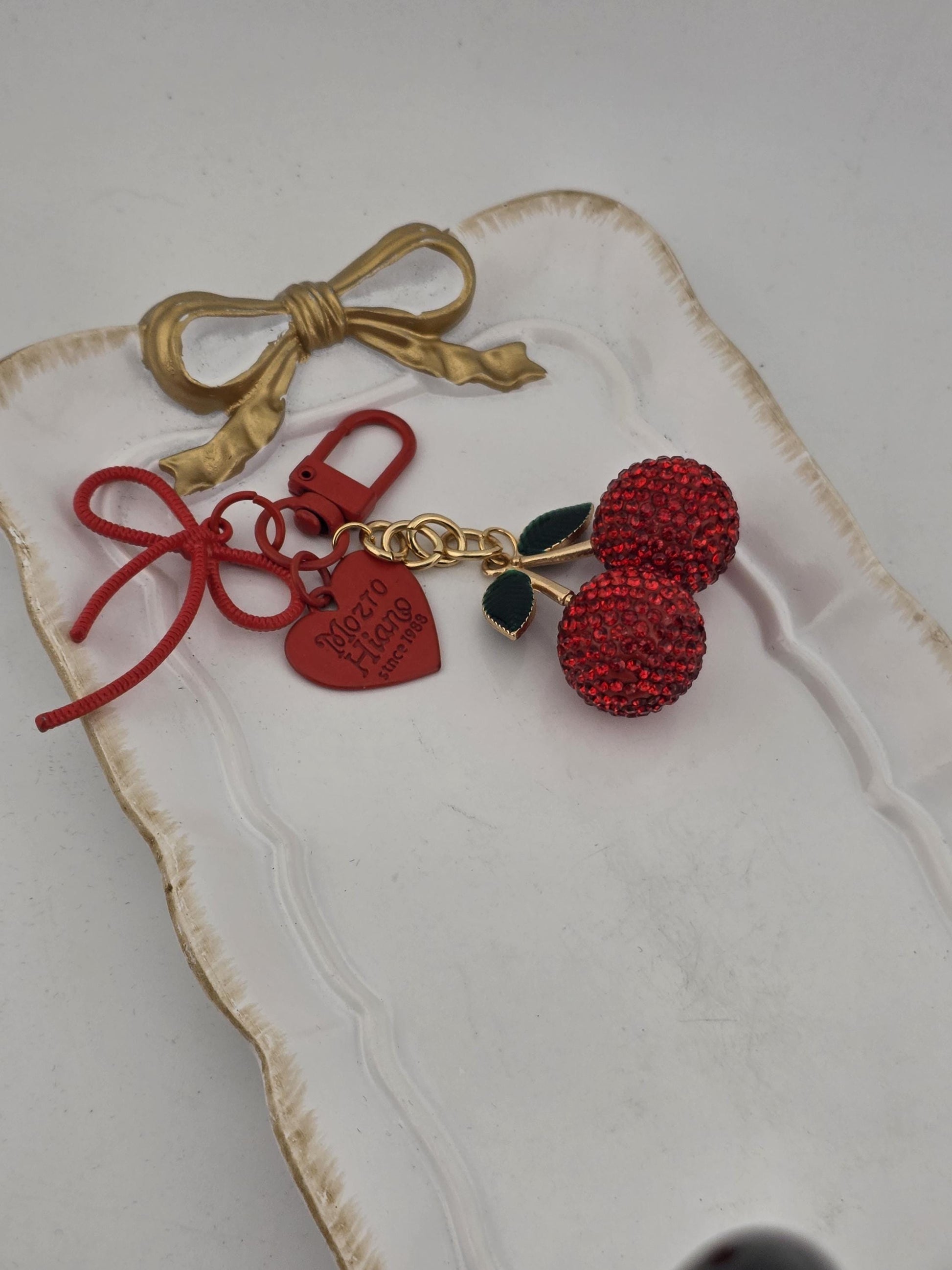 a white tray with a gold bow and a red charm bracelet with a keychain charm.