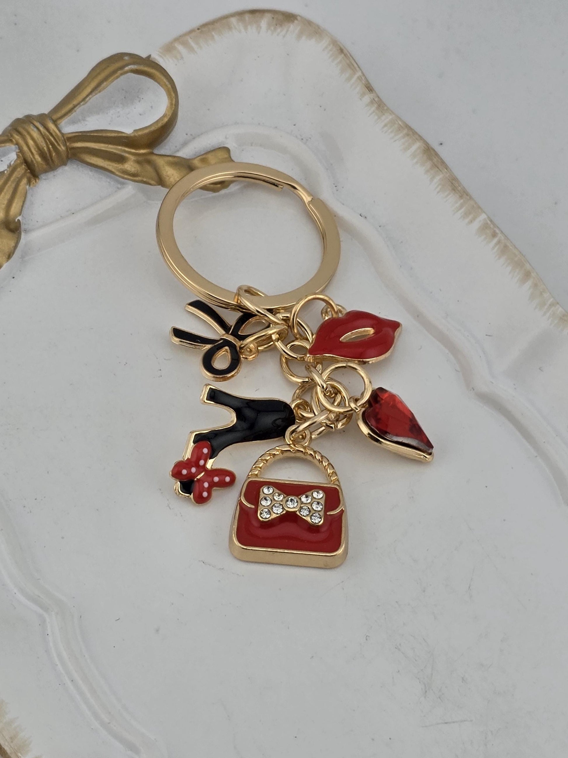 A decorative keychain with various charms, including a red flower, a red bow, and a red and gold butterfly, as well as a small red and gold bag.