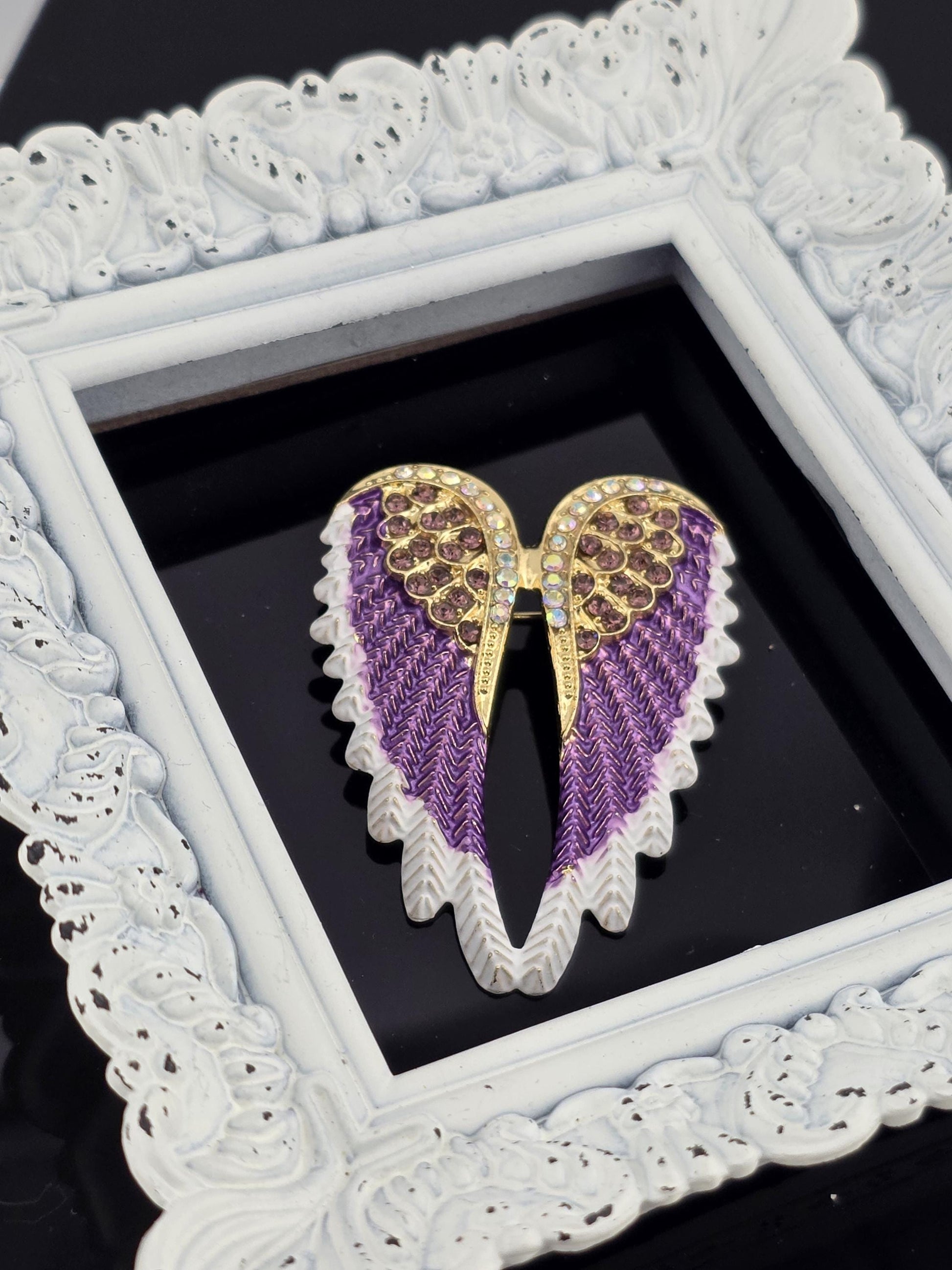A decorative white frame with a purple and gold wing-shaped object, possibly a piece of jewelry, displayed within it.