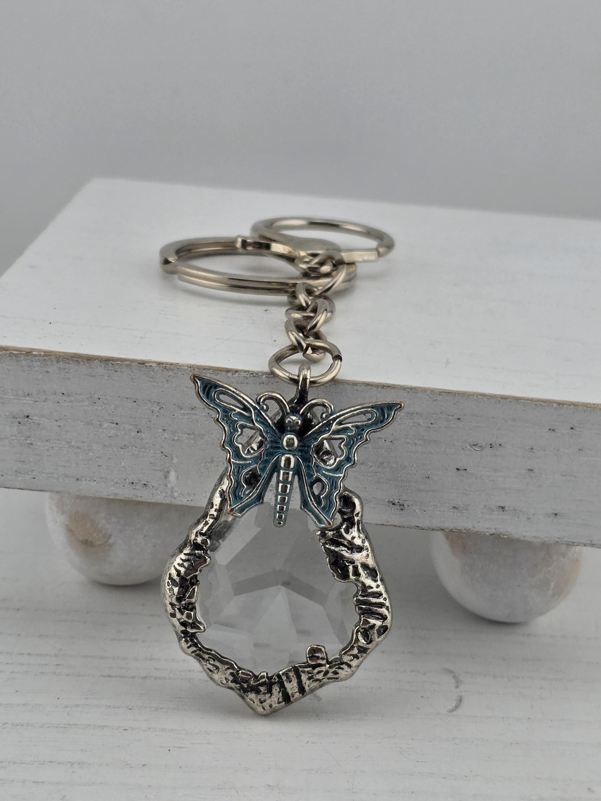 A silver keychain with a decorative butterfly design and a clear gemstone attached to it.