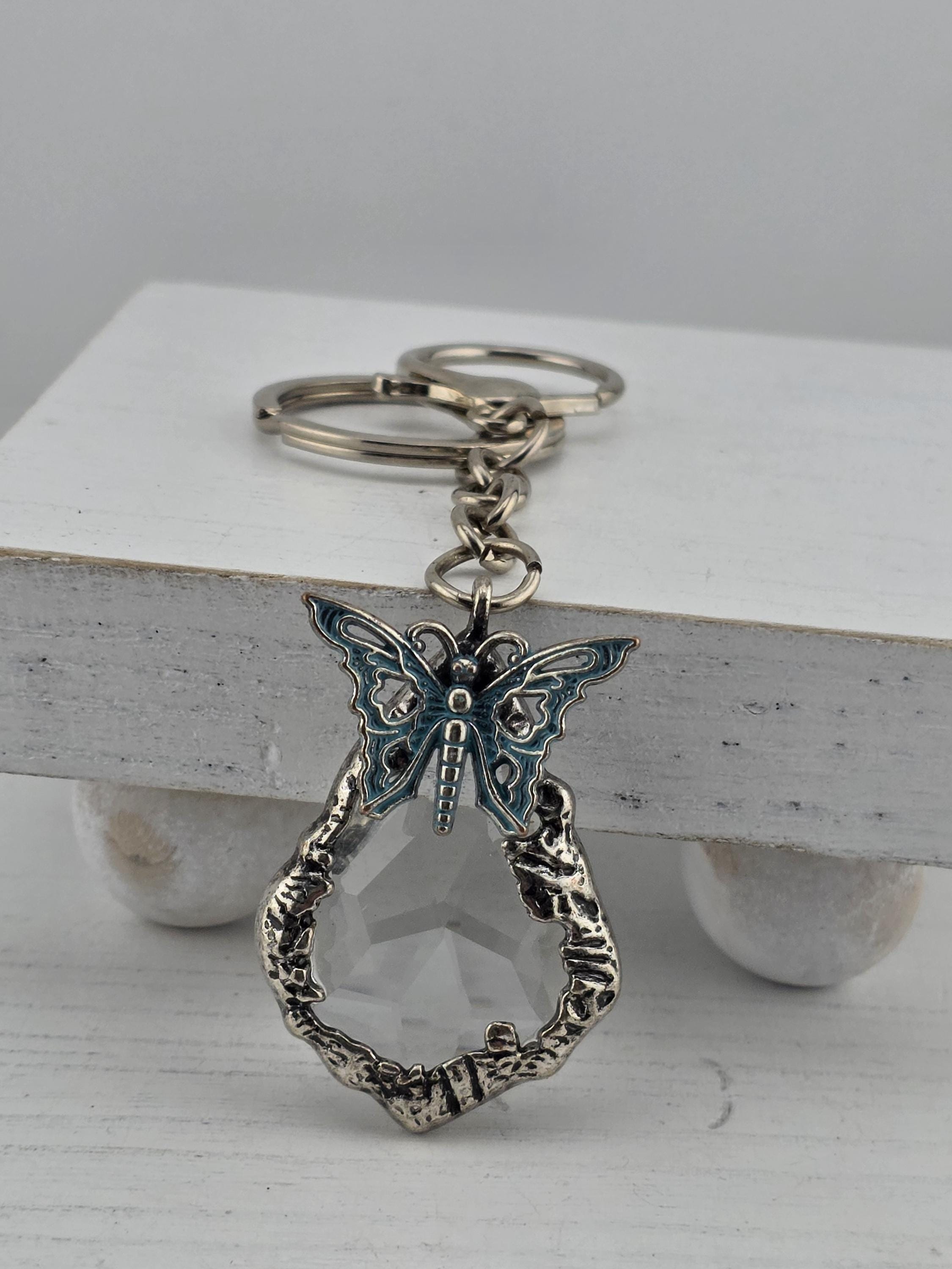 A silver keychain with a decorative butterfly design and a clear gemstone attached to it.