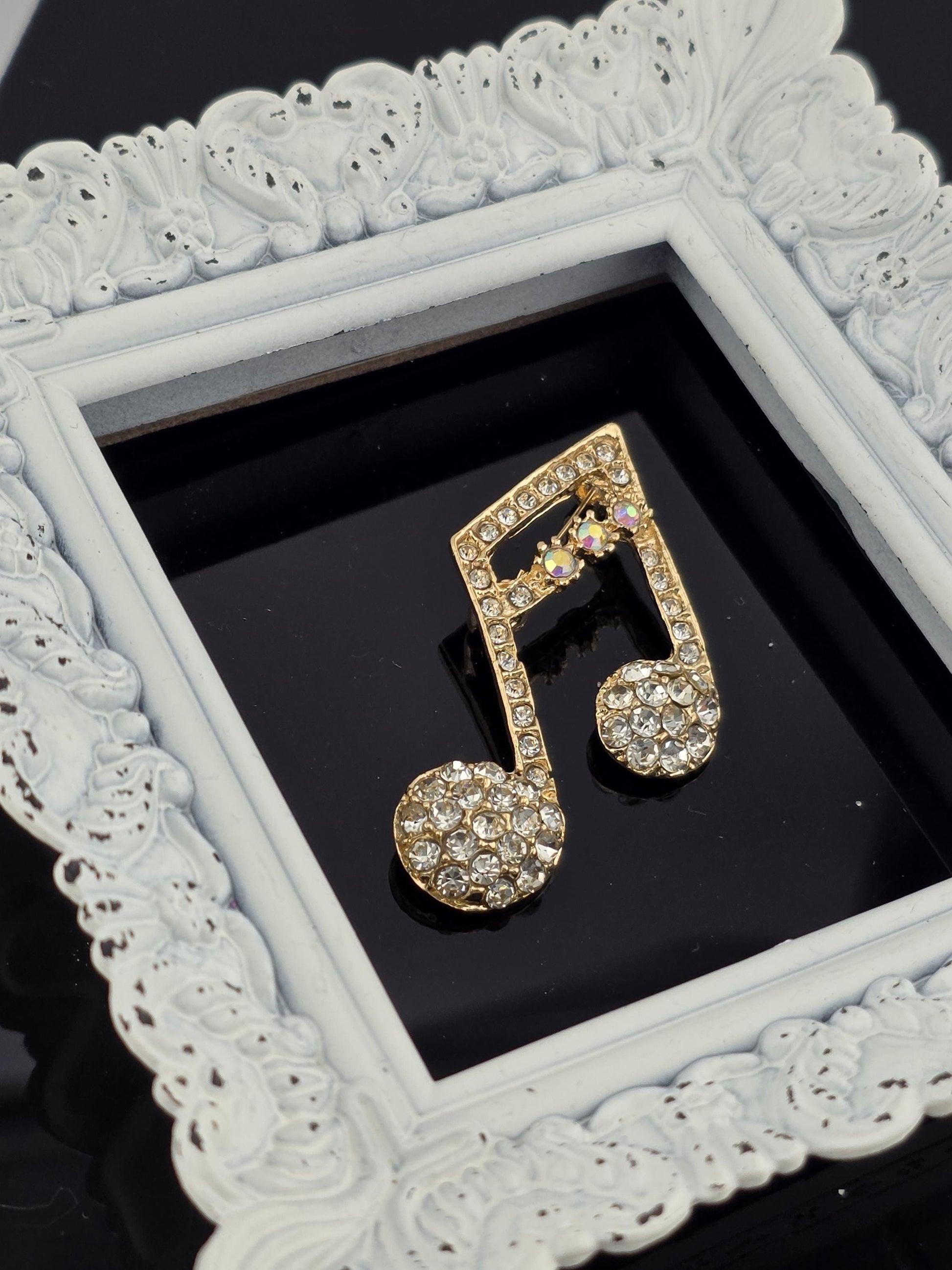 A white ornate frame with a gold-colored rhinestone-encrusted musical note design is displayed against a black background.