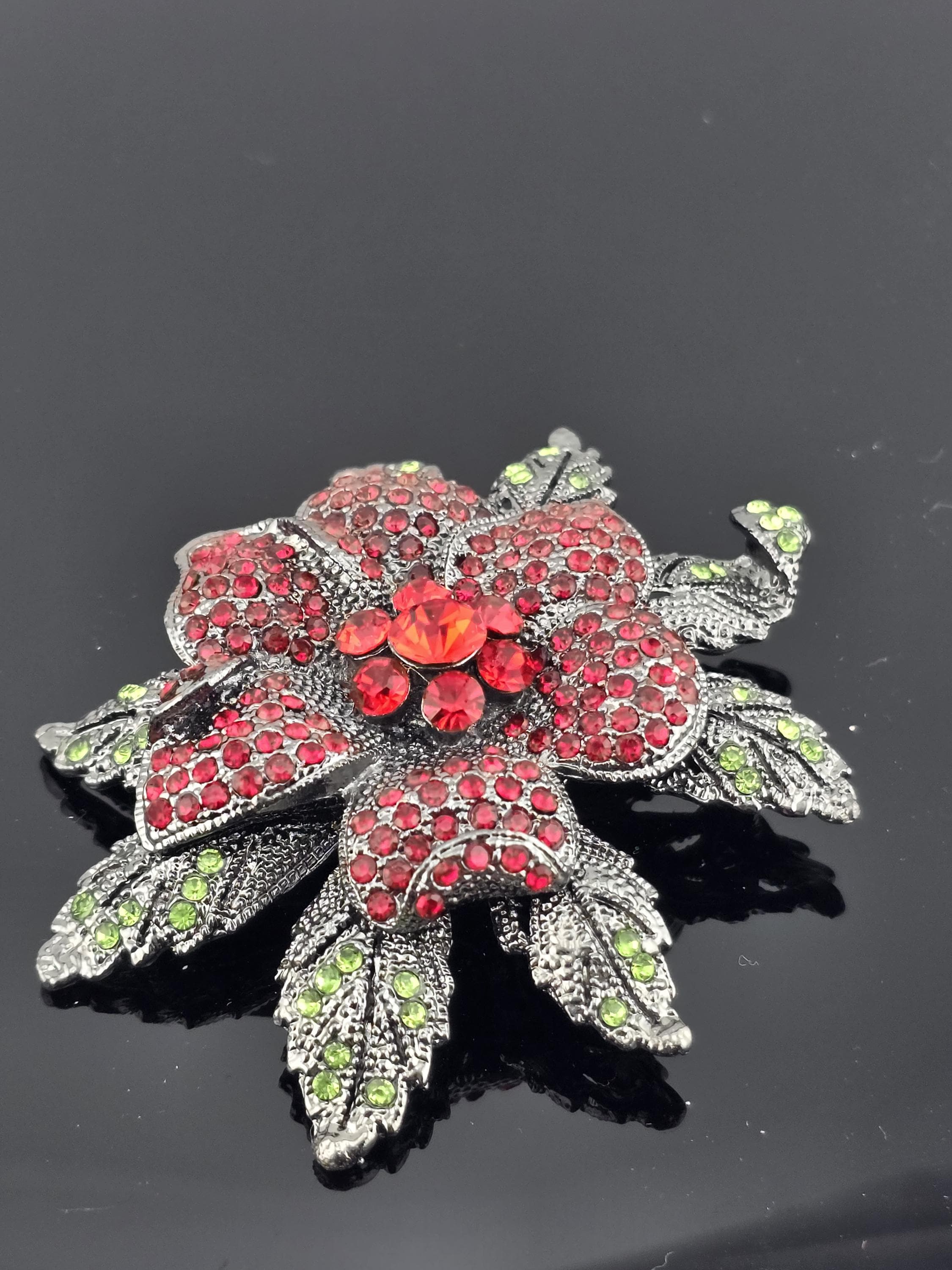 A decorative brooch with a flower-like design, featuring red gemstones and green gemstones.