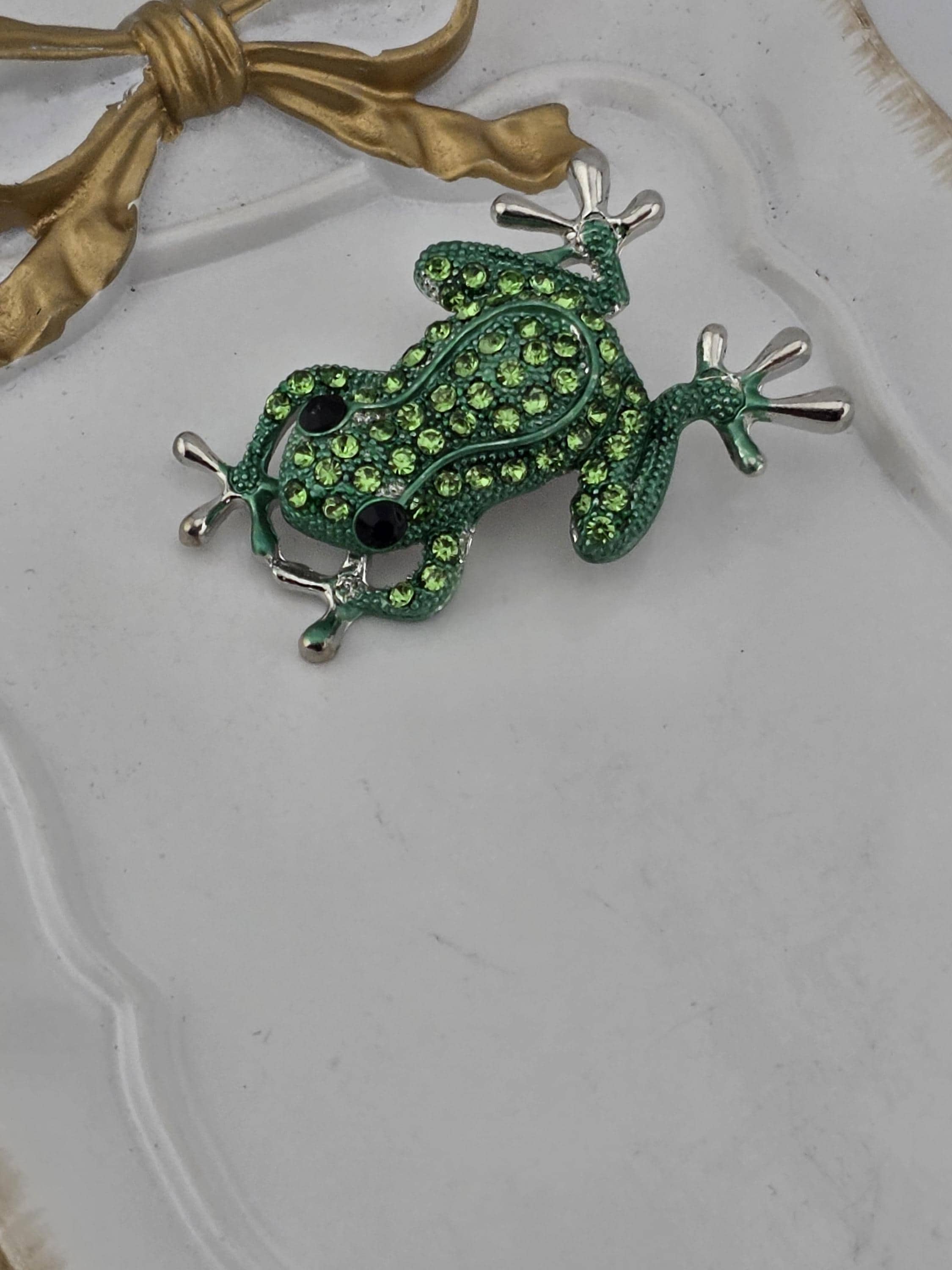 A green frog brooch with rhinestones is displayed on a white surface.