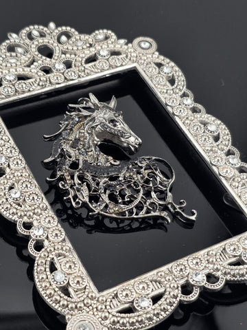 a decorative silver frame with a detailed design, including a central motif resembling a dragon or mythical creature.