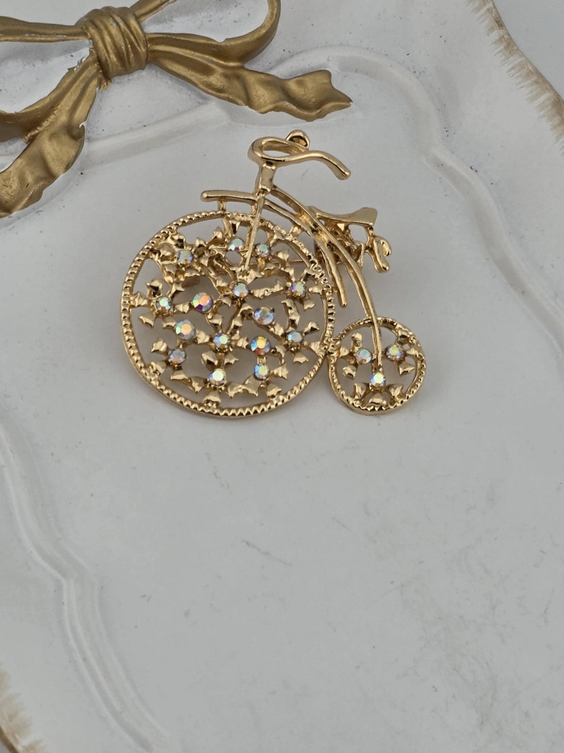A decorative gold-colored pendant with a floral design and small gemstones is displayed on a white surface.